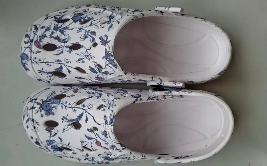 Weiße Clogs mit Blumenmuster und Belüftungslöchern, von oben gesehen, auf einer ebenen Fläche stehend. Weiße Clogs mit Blumenmuster und Belüftungslöchern, von oben gesehen, auf einer ebenen Fläche stehend.