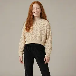 Mädchen trägt einen beigen Strickpullover und schwarze Hose vor hellem Hintergrund. Mädchen trägt einen beigen Strickpullover und schwarze Hose vor hellem Hintergrund.