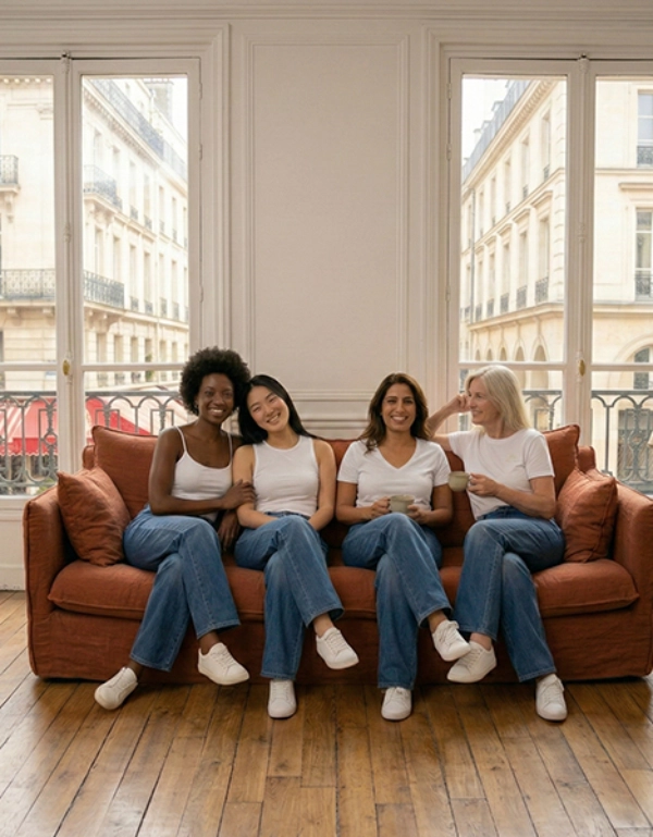 Vier Personen in passenden Outfits sitzen auf einem gemütlichen Sofa und genießen Getränke in einem hellen Raum mit Fenstern und Blick auf die Stadt.