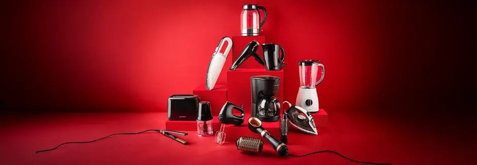 Eine Vielzahl von Küchen- und Schönheitsgeräten, darunter ein Wasserkocher, ein Mixer, ein Staubsauger und Haarstylinggeräte, sind auf roten Blöcken angeordnet.