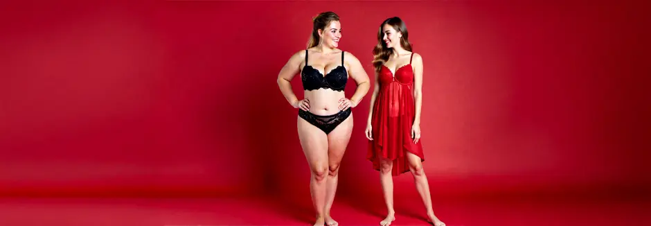 Zwei Frauen posieren vor einem leuchtend roten Hintergrund, eine in schwarzer Dessous und die andere in einem durchsichtigen roten Nachthemd.