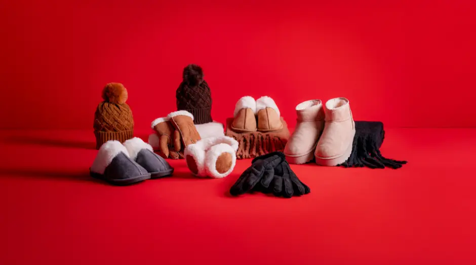 Gemütliche Winteraccessoires: Hausschuhe, Handschuhe, ein Schal und Mützen, arrangiert vor einem leuchtend roten Hintergrund.