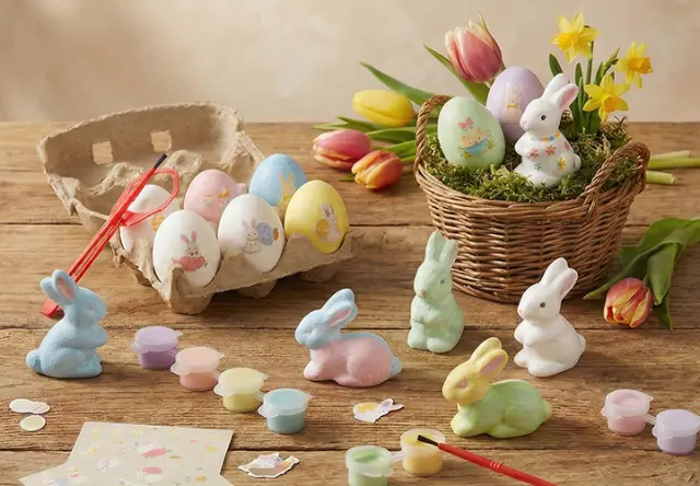 Farbenfrohe Osterdekorationen mit bemalten Eiern, pastellfarbenen Hasen und Malutensilien auf einem rustikalen Holztisch mit Blumen. Farbenfrohe Osterdekorationen mit bemalten Eiern, pastellfarbenen Hasen und Malutensilien auf einem rustikalen Holztisch mit Blumen.