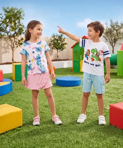 Mädchen und Junge in farbenfrohen Shirts spielen gemeinsam im Park – sommerliche Kindermode für Alltag und Freizeit